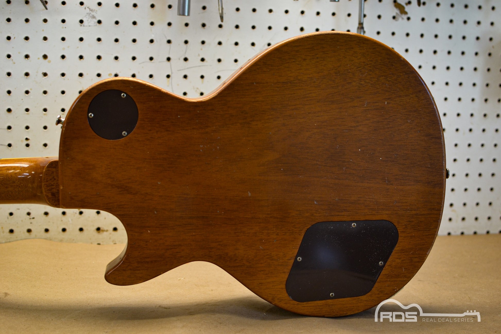 Wooden electric guitar body on a pegboard background