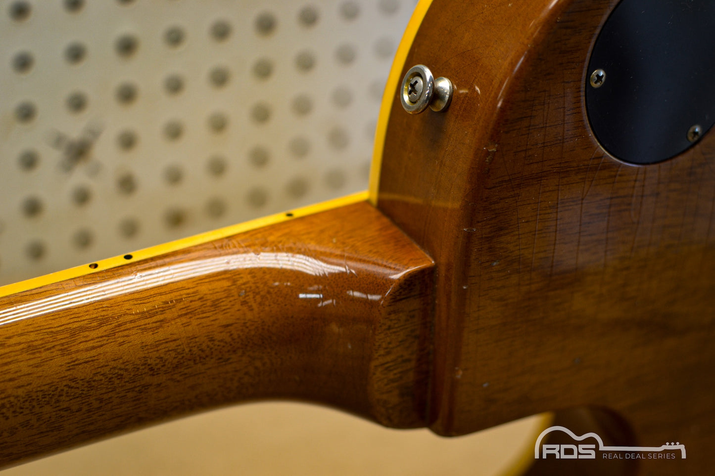 Close-up of a wooden guitar neck with a pegboard background