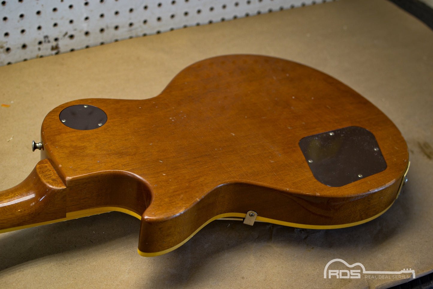 Wooden guitar body on a workbench with a pegboard in the background
