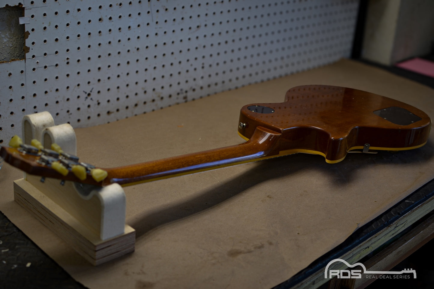 Partial view of a guitar on a stand with a pegboard background