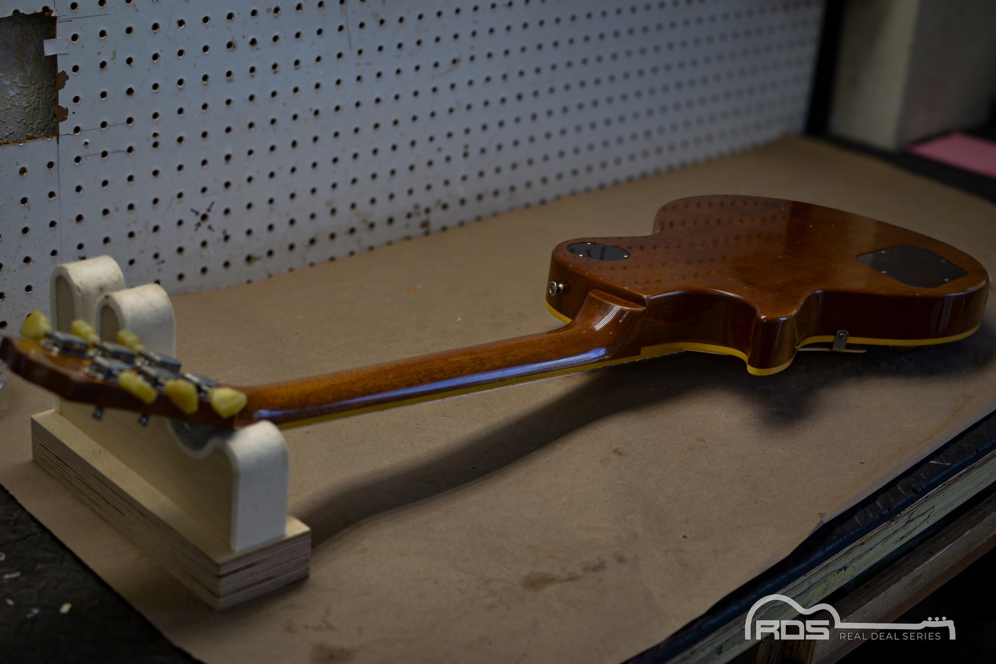 Partial view of a guitar on a stand with a pegboard background