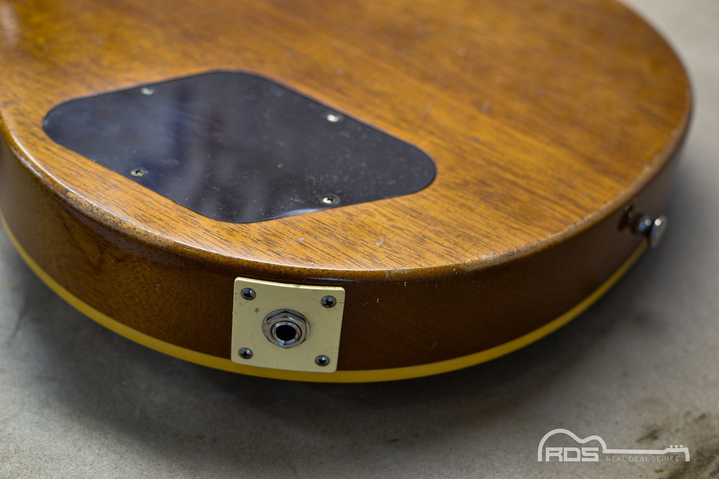 Close-up of a wooden guitar body with a visible brand logo in the corner.