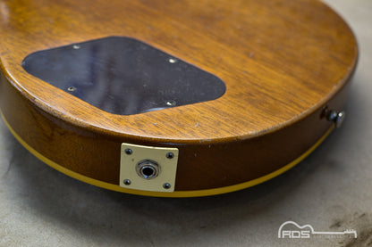 Close-up of a wooden guitar body with a visible brand logo in the corner.